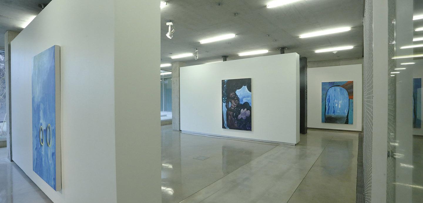 Three white walls with large paintings hung on each panel.
