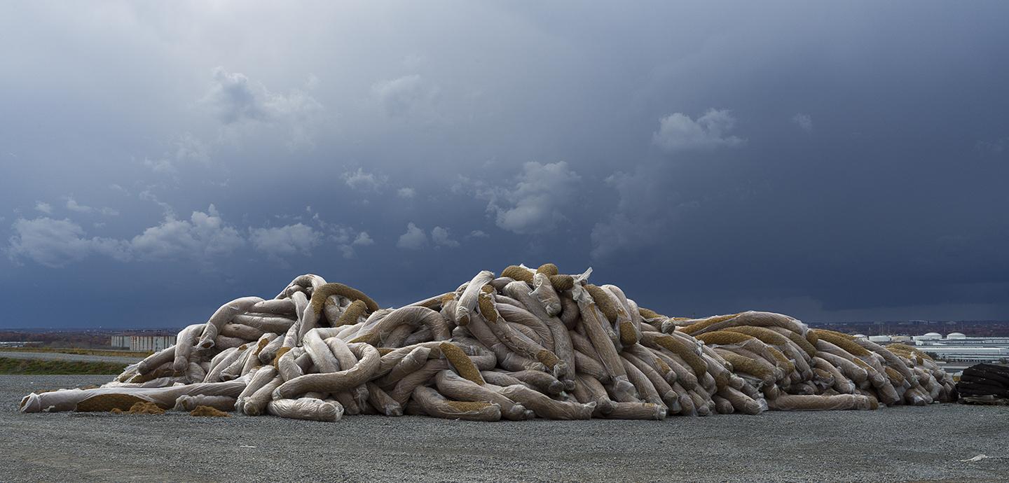 Partially wrapped tubes with some yellow materials exposed on the ground in front of a stormy sky.