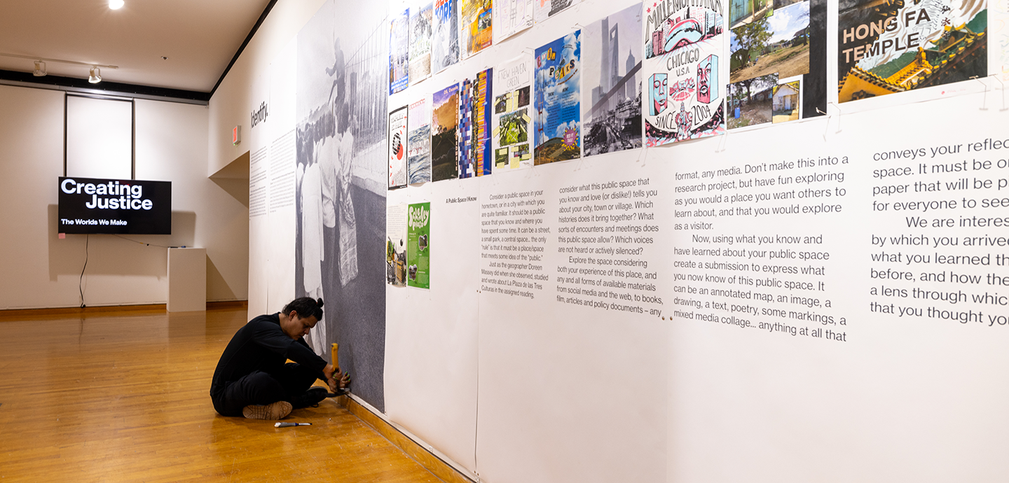A person sitting on the floor pinning artwork to a gallery wall.