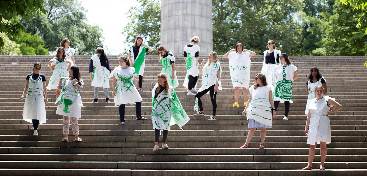 A group of women standing on stone steps. They are wearing white sheets colored with green