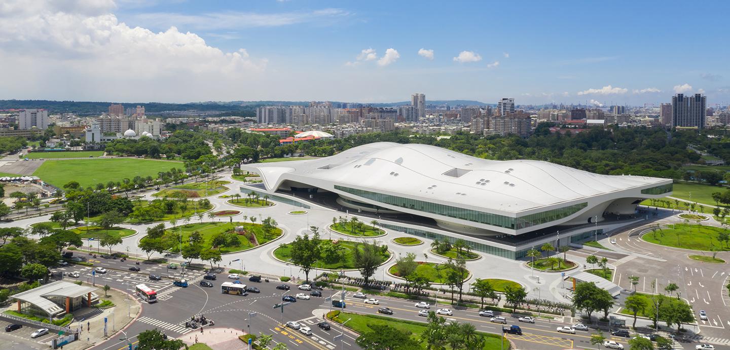 The exterior of a large modern building situated adjacent to a city scape. 