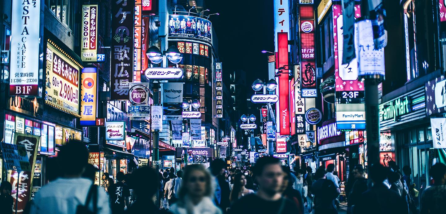 Retail stores in a Japanese city lit up at night along a street crowded with pedestrians