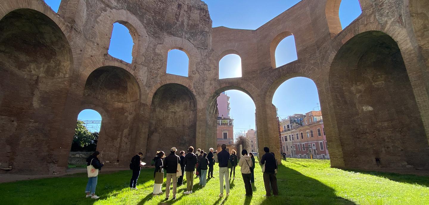 A group of peopel stangin on short green grass surrounded by massive stone structures.