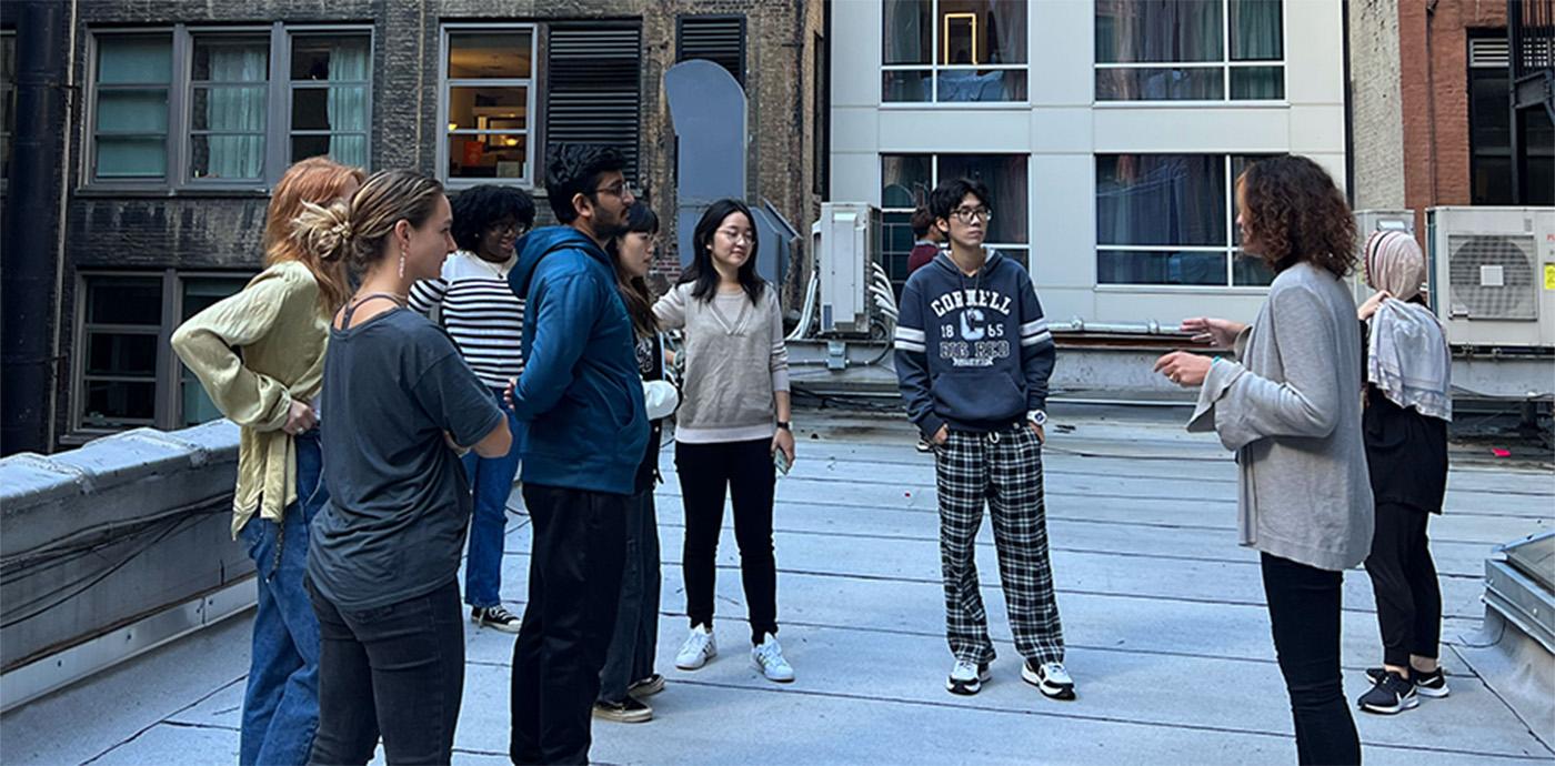 Woman talking to a group of students on a roof top in a city.