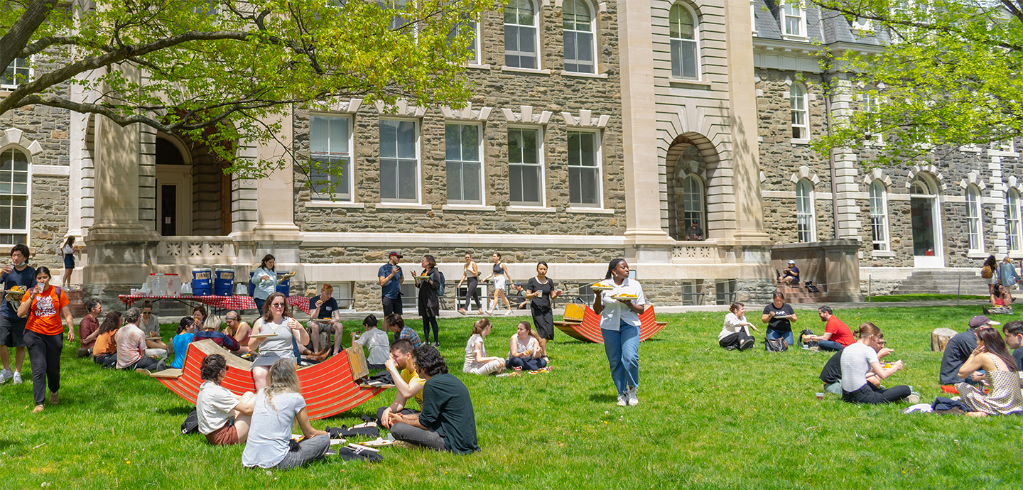 A group of student sitting in a circle on the grass eating hamburgers together.