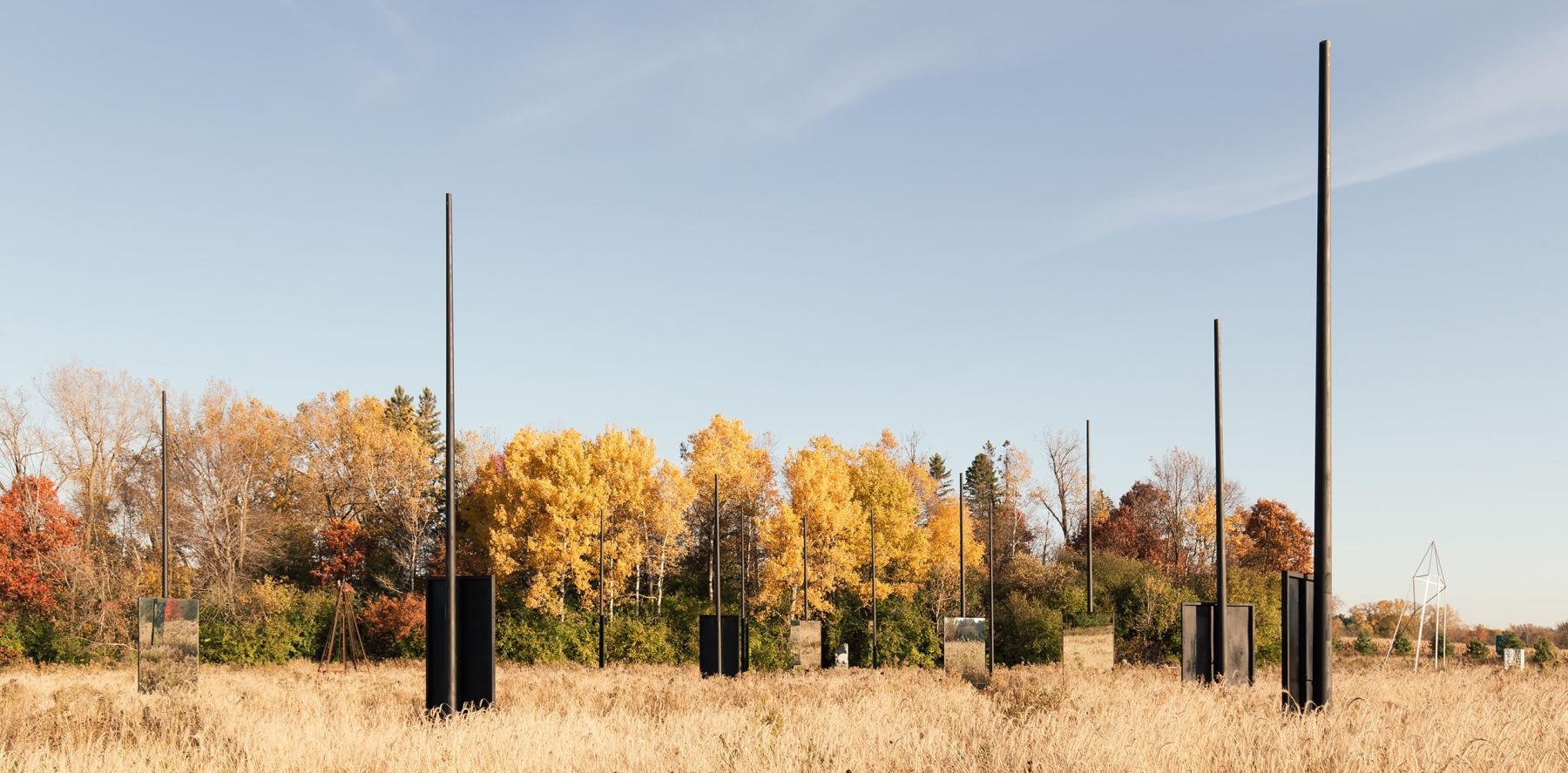 Upright poles and rectangular blocks in a field of dry grass with trees behind.
