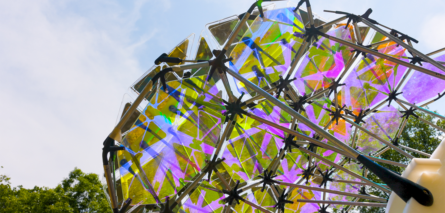Large holographic panels constructed into a single structure with a bright blue sky in the background.