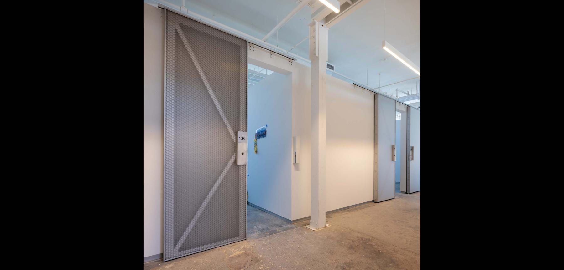 White hallway with metal door on concrete floor.