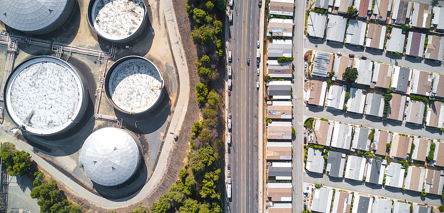 Houses in a row with giant white silos across and adjacent to a busy street 