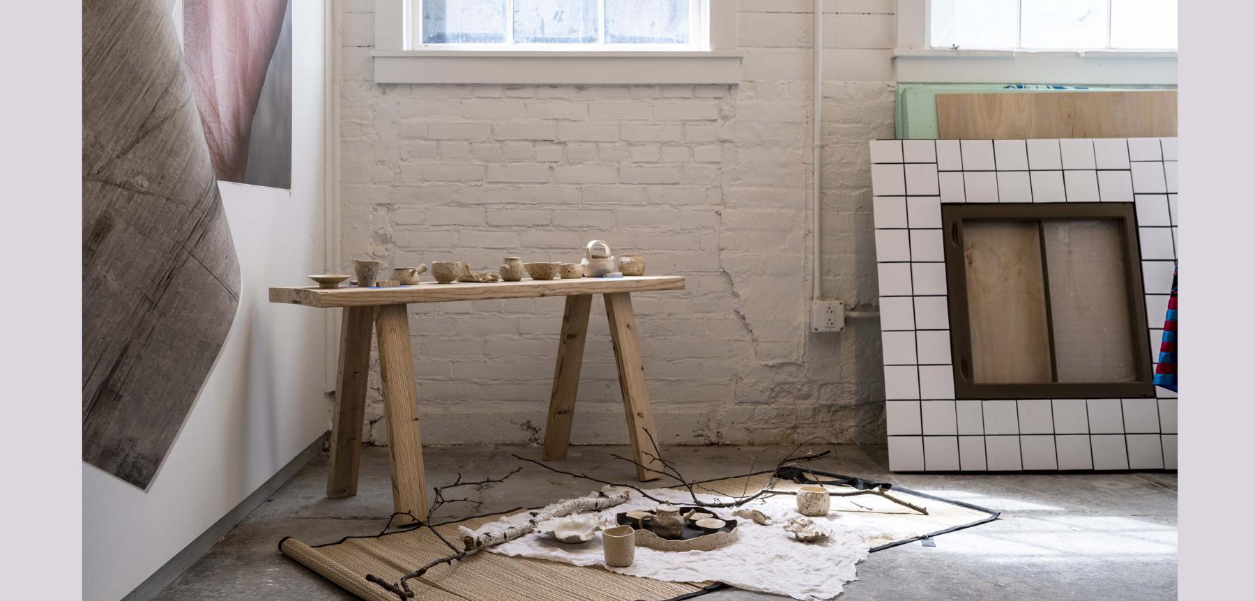 Various small hand crafted bowls on a small wooden table with various artworks on the ground.