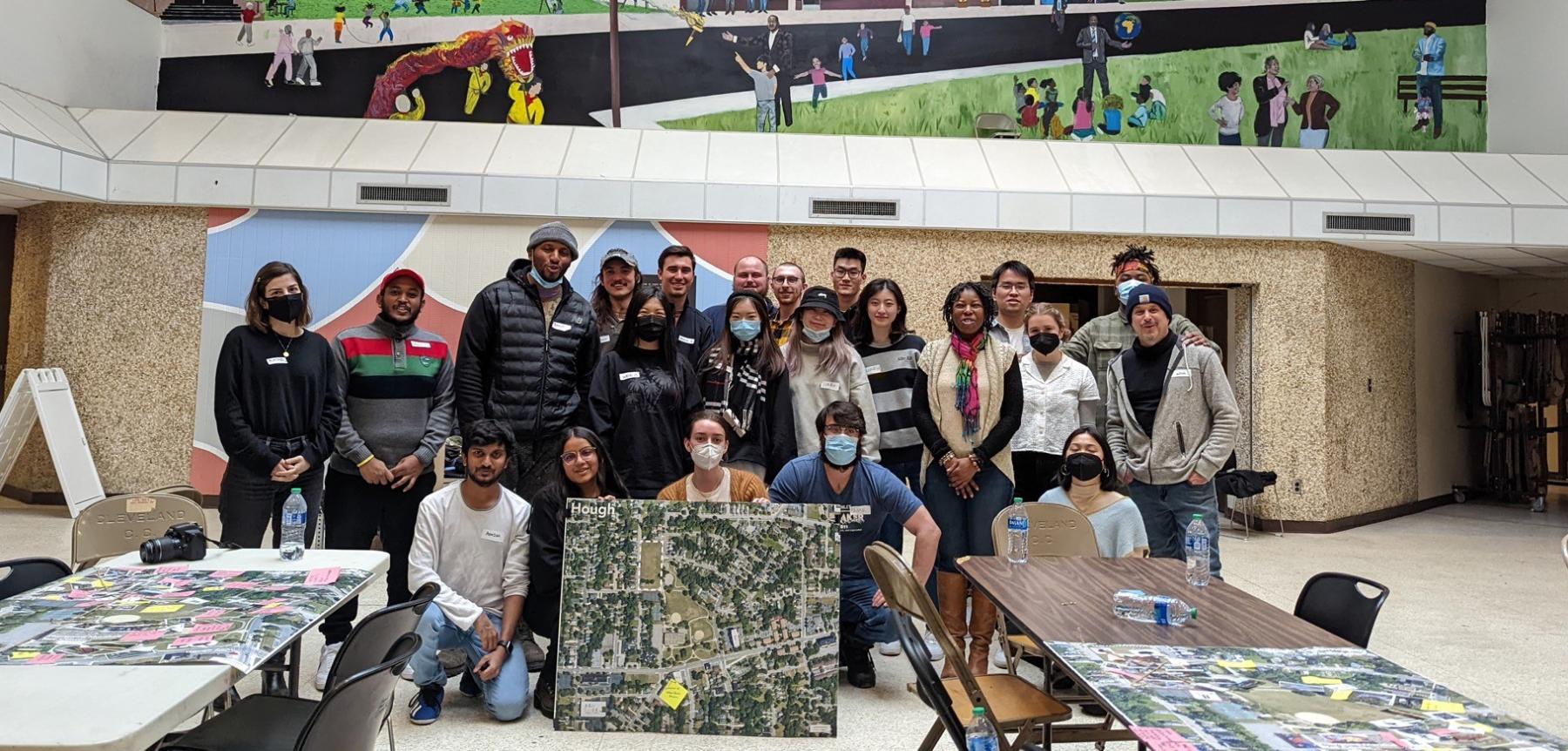class group, teacher and project partners posing with city plans indoors with tables and chairs