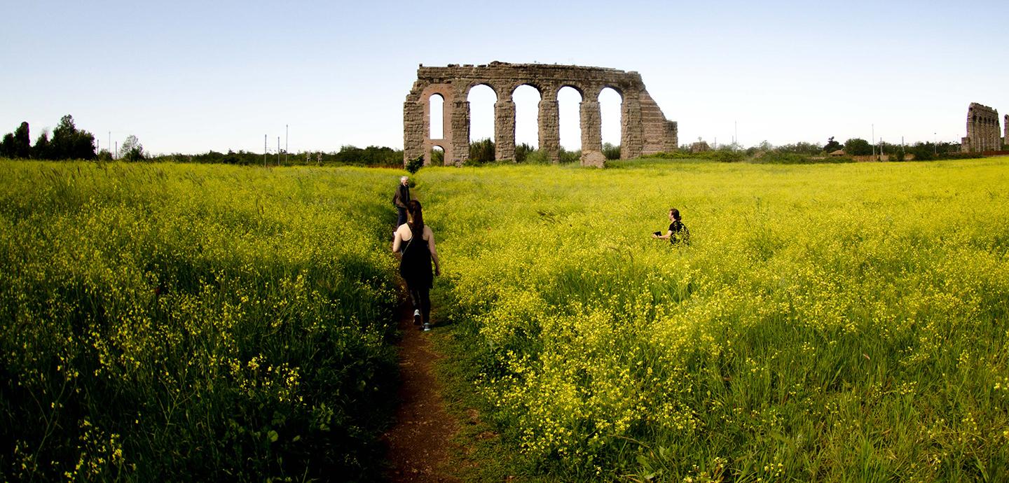 Two students and a professor in front of the Parco degli Acquedotti ruins.