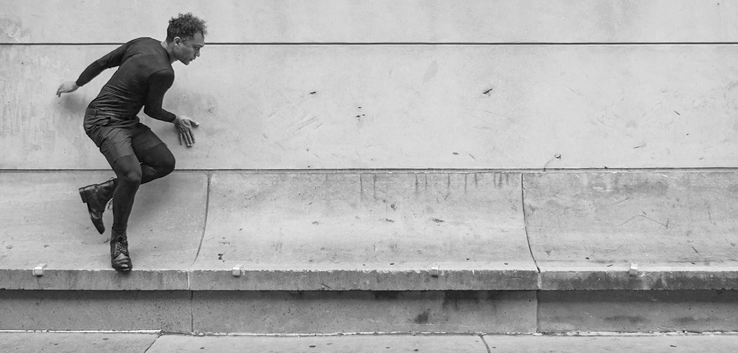 black and white image of a man jumping from a stone bench