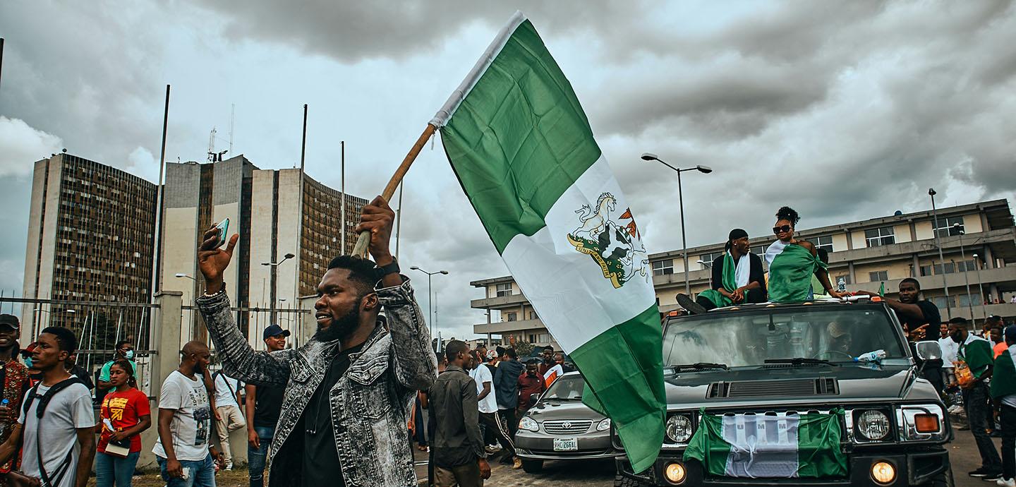Man holding a Nigerian flag and leads a group of protesters