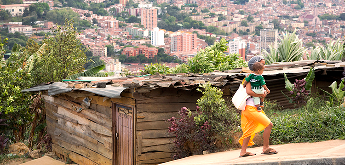 woman carrying a child walking on a sidewalk with dense buildings in the background