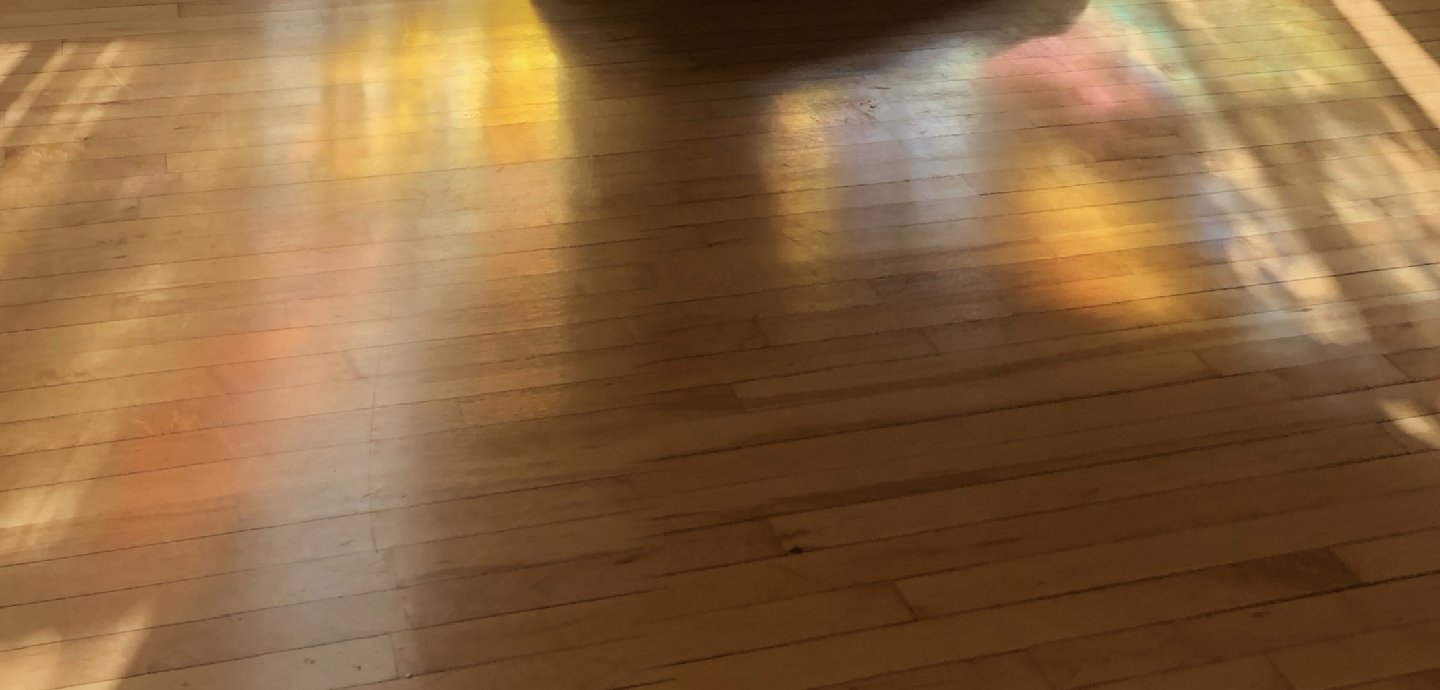A photo of a wood floor with hazy, faintly rainbow splotches of light and contrasting shadows