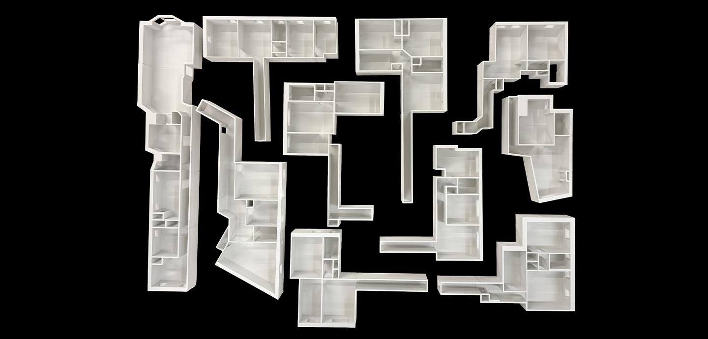 Top-down view of white models depicting residential rooms arranged in a grid on a black background.