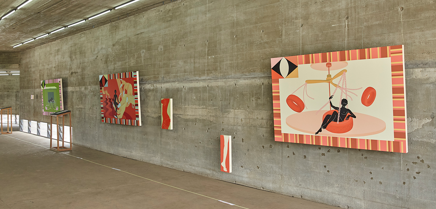Paintings hung on a concrete wall feature dark-skinned subjects bordered by orange, yellow, and cream colored stripes. 