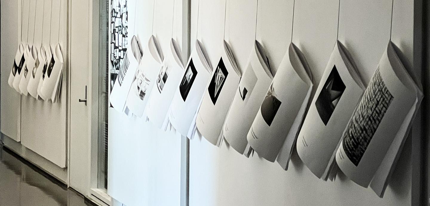 15 large booklets are hung in a row each by their top left corner.