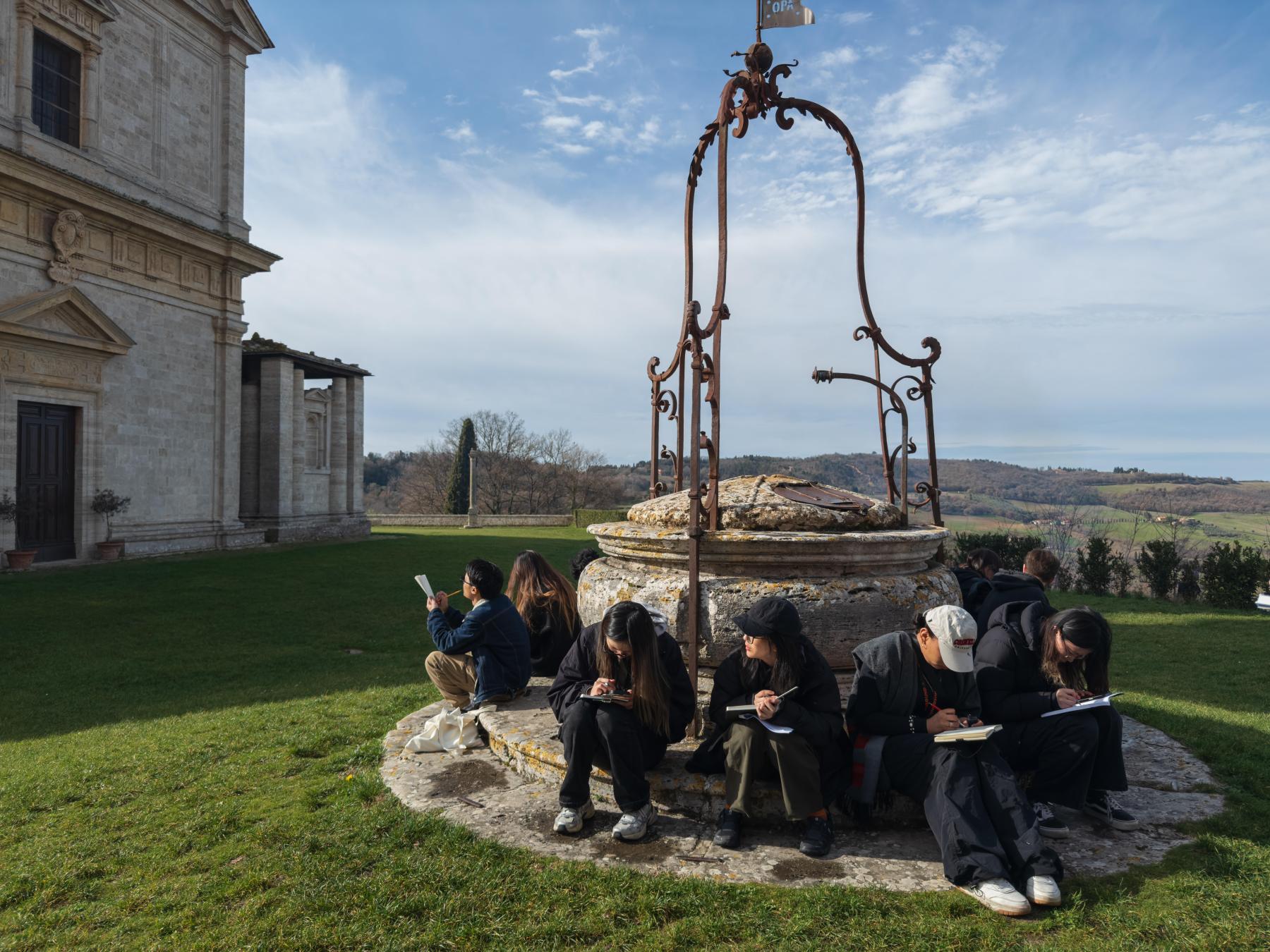 students sitting around an old well in Italy drawing an historic building