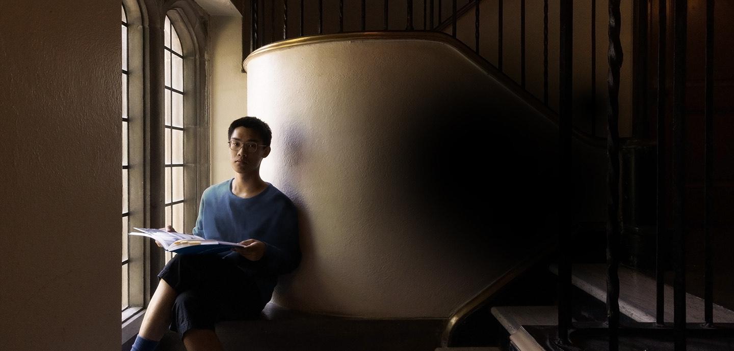 Person sitting in stairwell with papers on their lap, staring at the camera