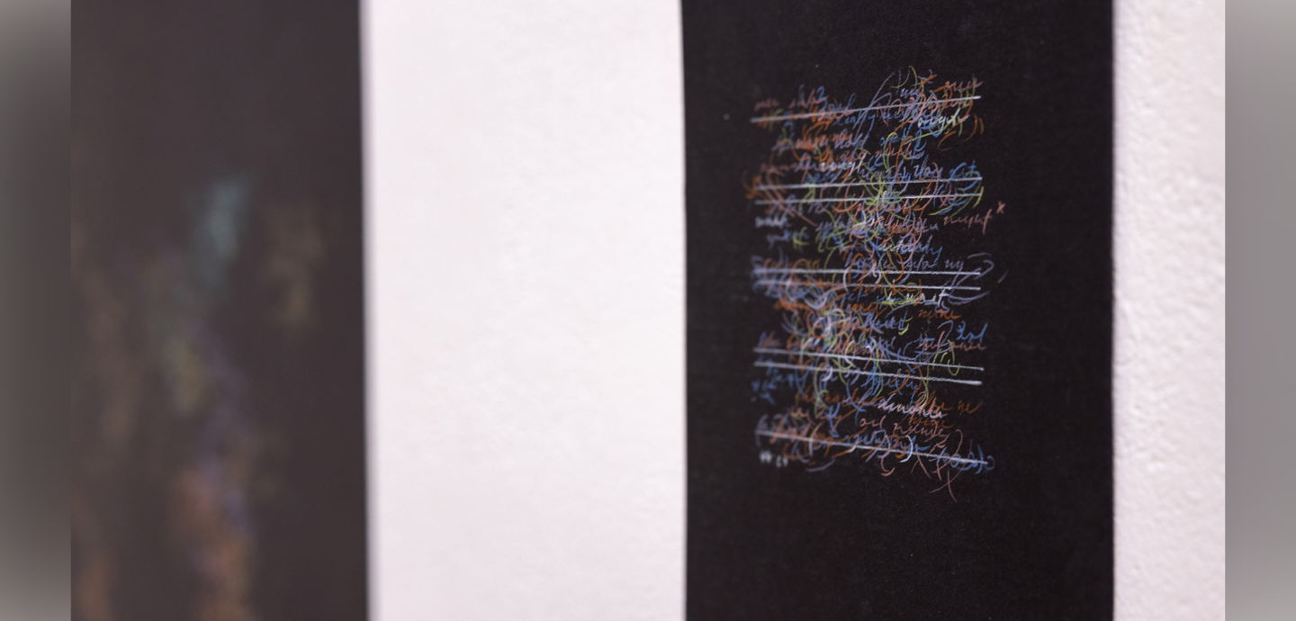 Black canvas hung on a white wall with colorful non-descriptive writing in the middle.