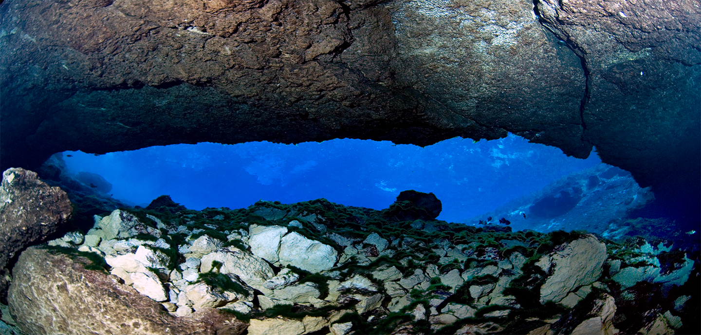 Underwater cave with rock rubble at the base of the cave and a narrow horizontal opening peering into the cave.