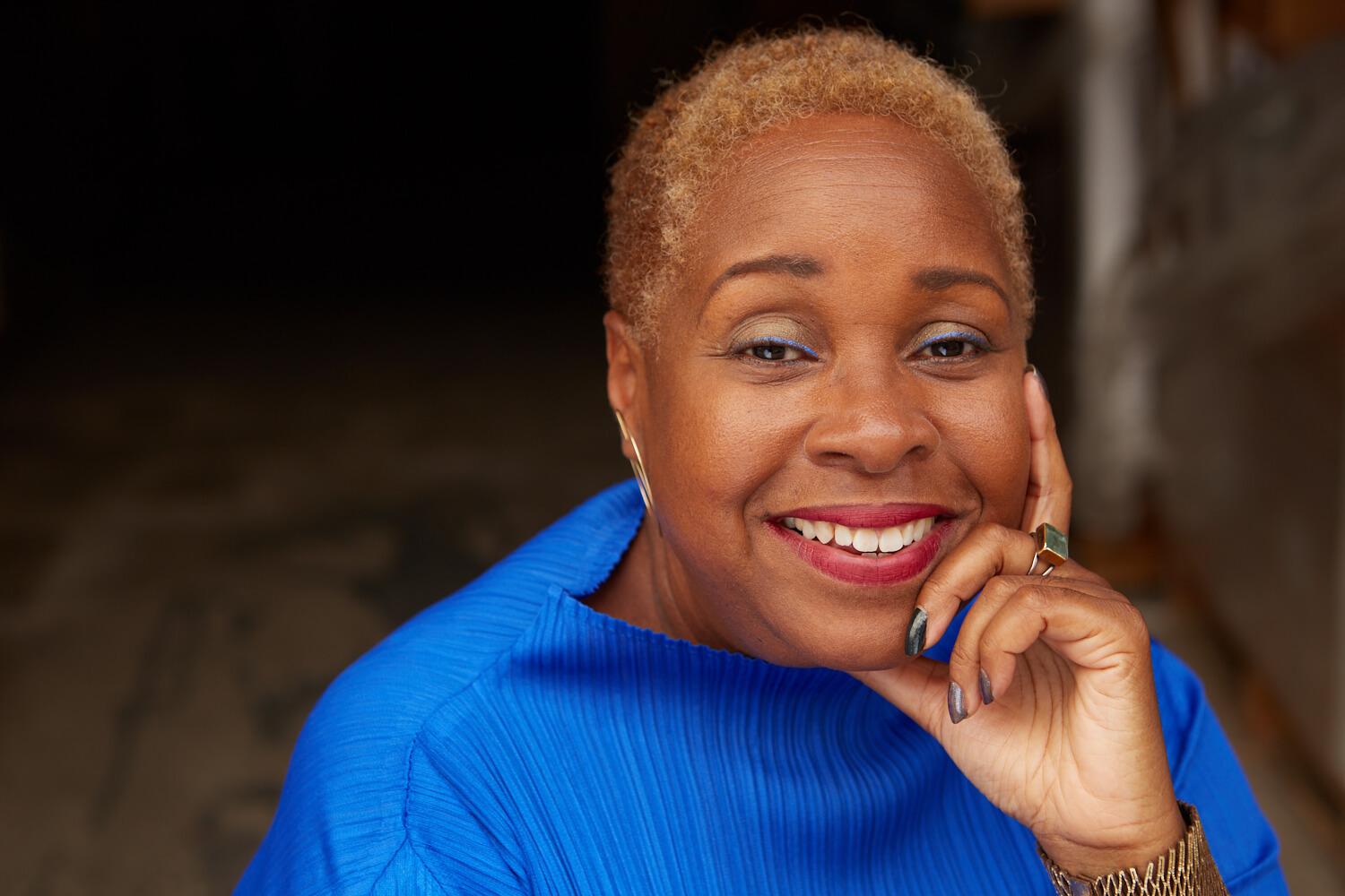 A Black woman wearing a blue shirt with her hand resting on the side of her face.