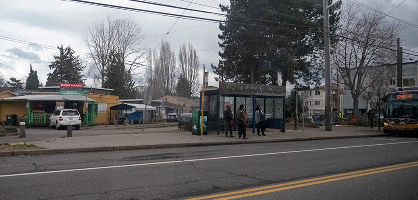 Three people waiting at a bus stop in a neighborhood on a grey, cloudy day.