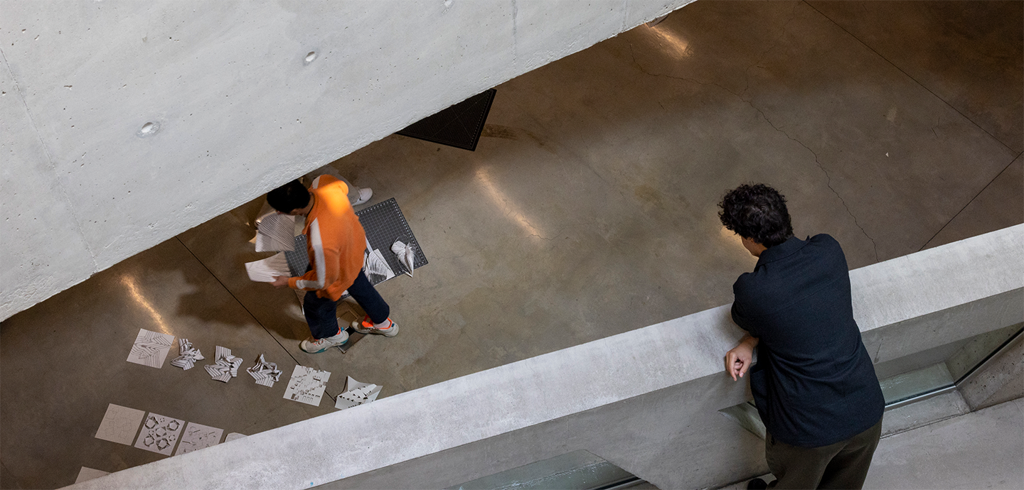 a person standing on a concrete bridge looking at another person setting up artwork on the floor