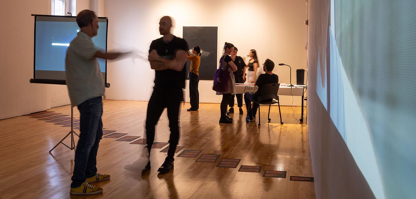 Seven people in a dark gallery viewing projections on the walls and work on the floor.