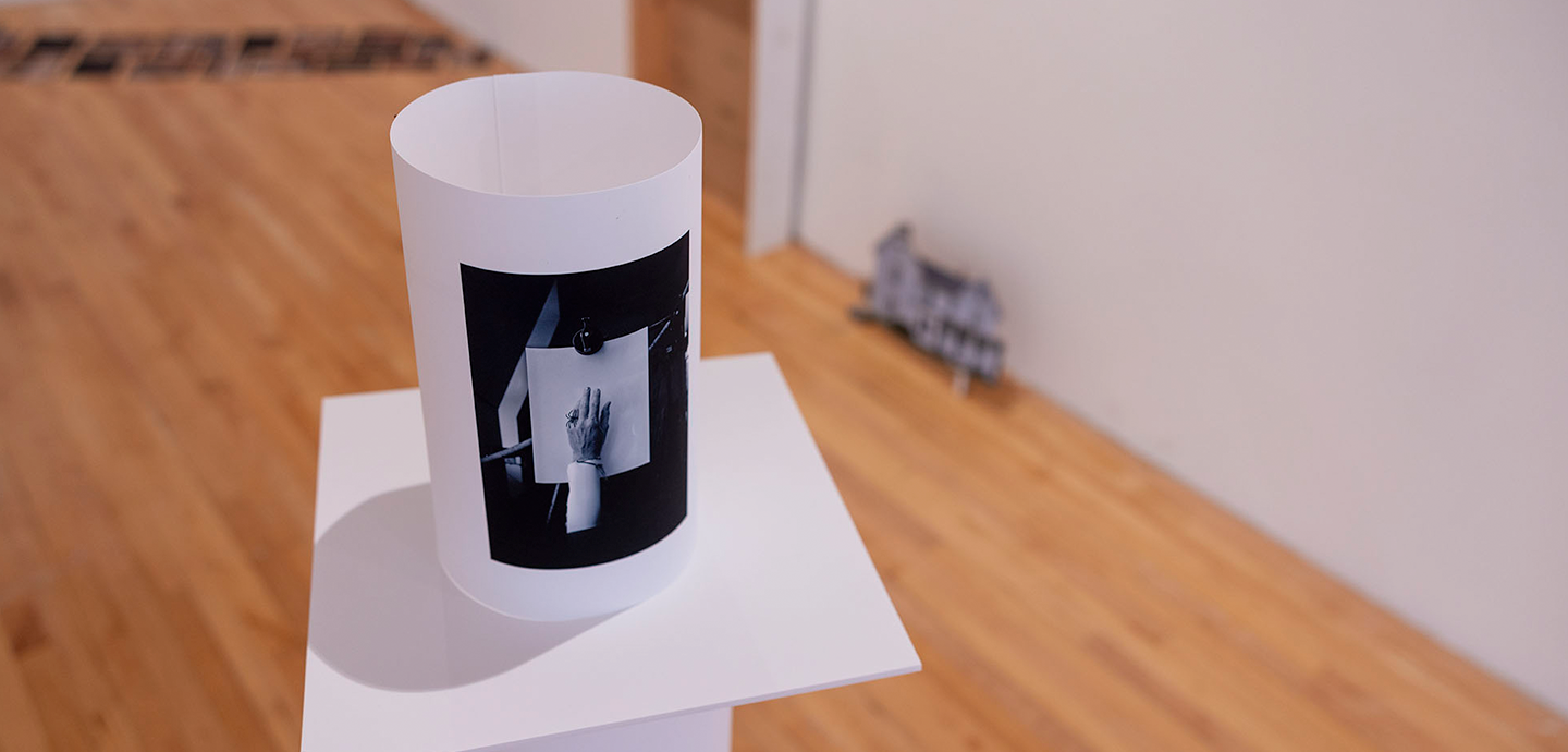 Black and white rolled image on a white pedestal in a gallery.