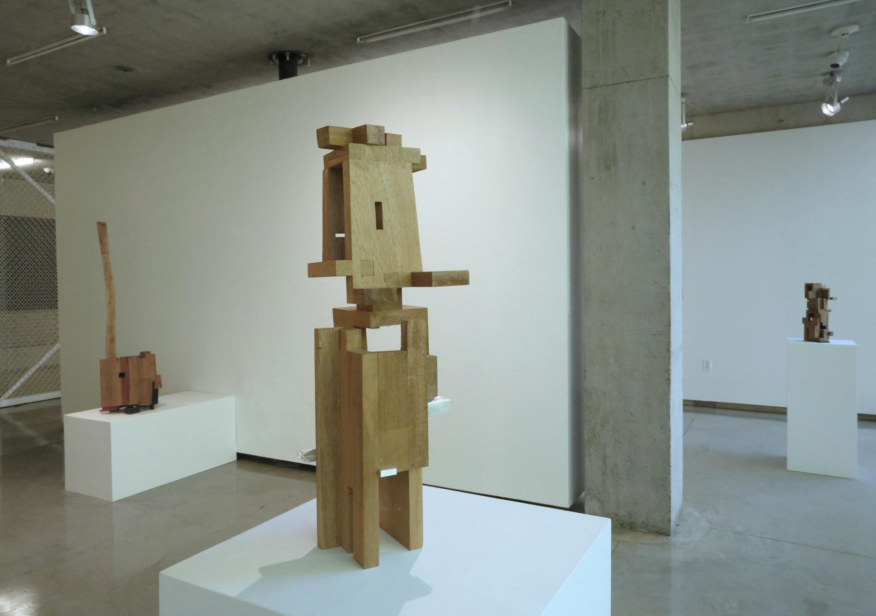 Abstract wooden sculpture piece with various sized rectangular pieces put together displayed on white pedestals. 
