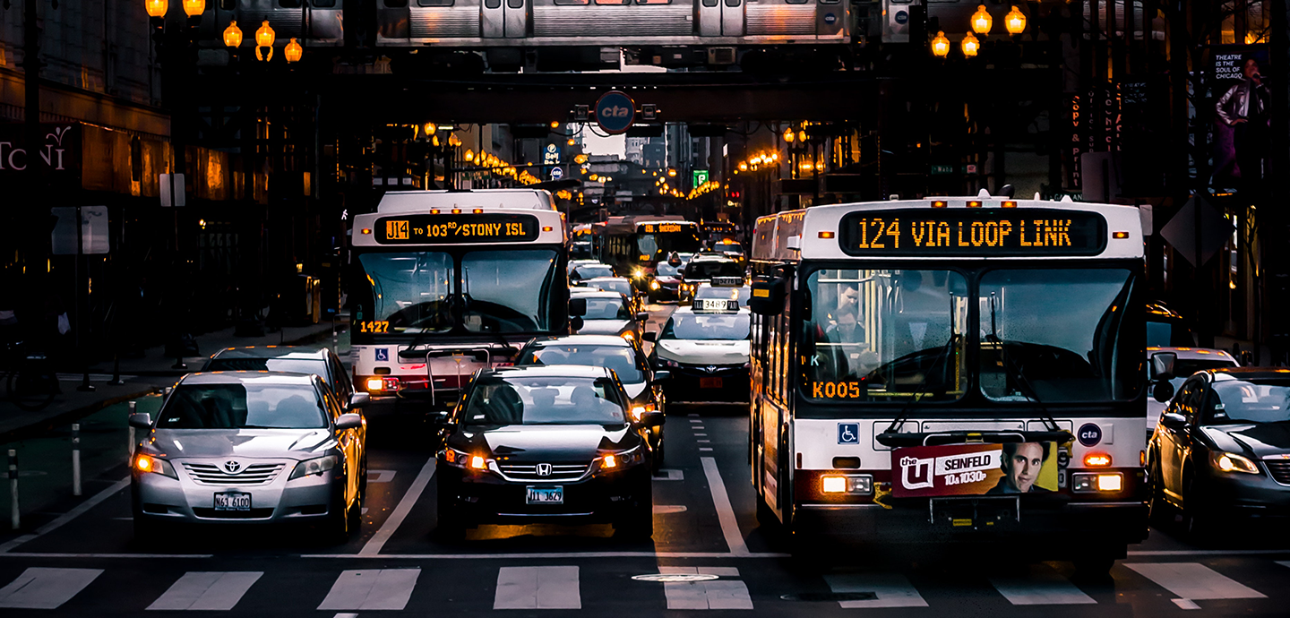 photo of street with buses and cars with subway over bridge