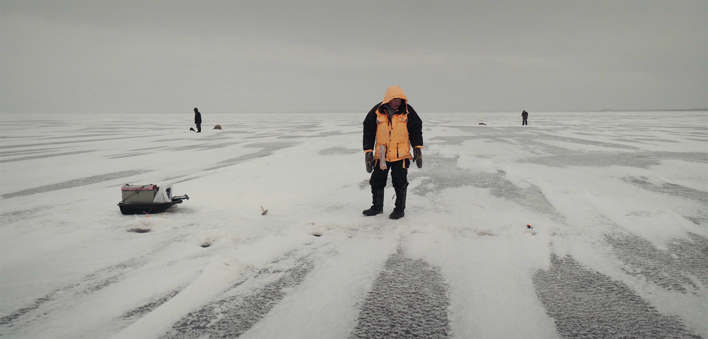 A man standing in a flat, desolate, and expansive snow covered environment.