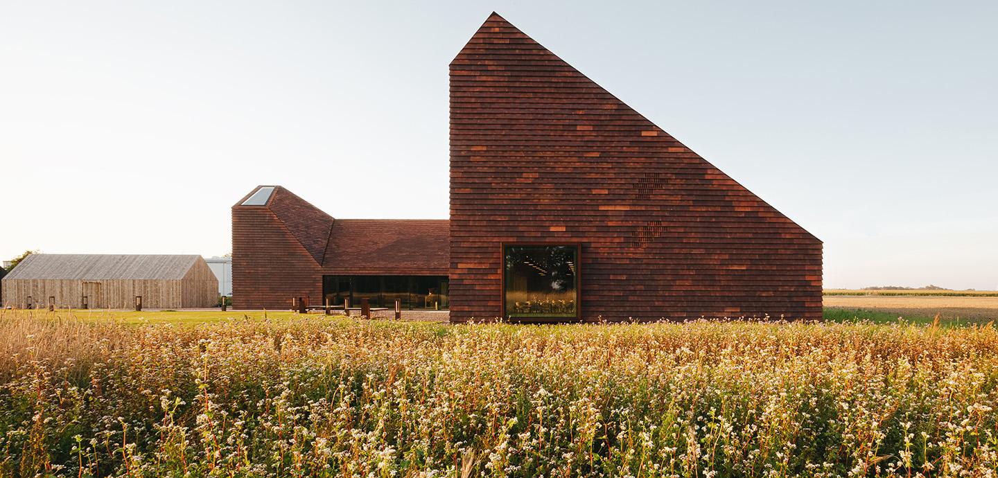 A modern brick structure situated in a field of golden and green toned plant life. 