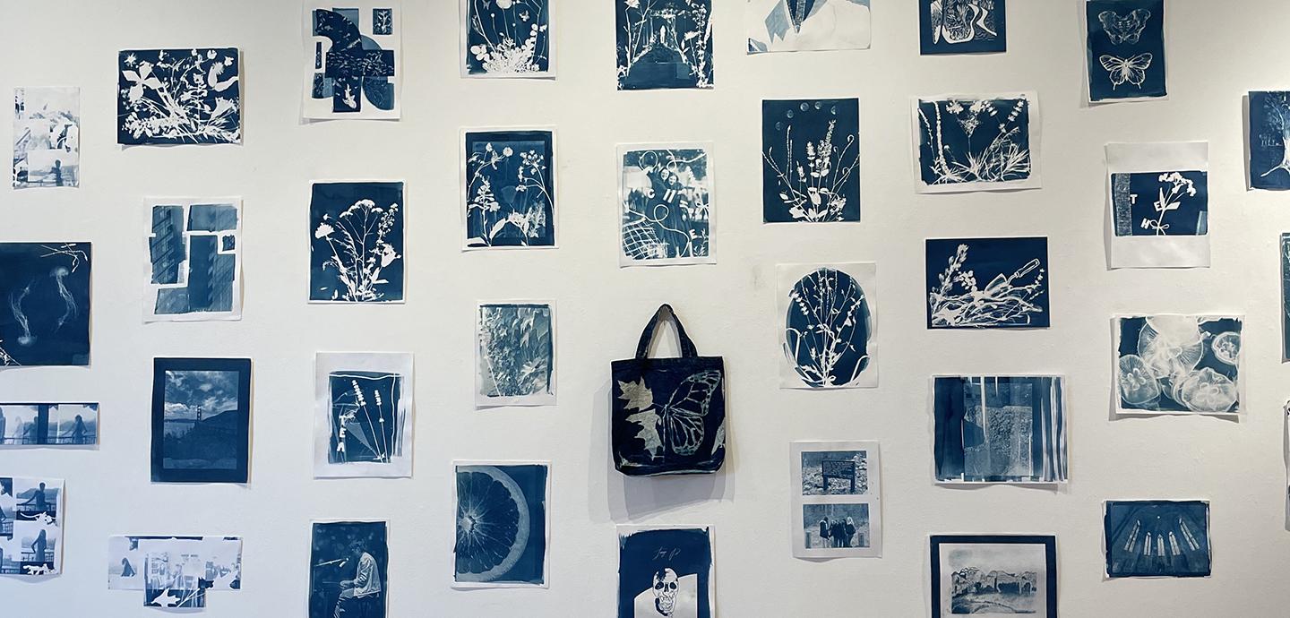 A collection of numerous blue and white prints on a white wall, with a similarly colored tote bag hanging in the middle.