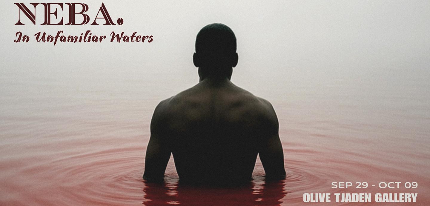 A shirtless man standing in waist-deep red water, his back turned to the camera.
