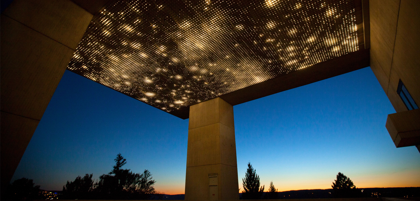 Concrete pillars connected to a light panel with a sunset and silhouetted trees