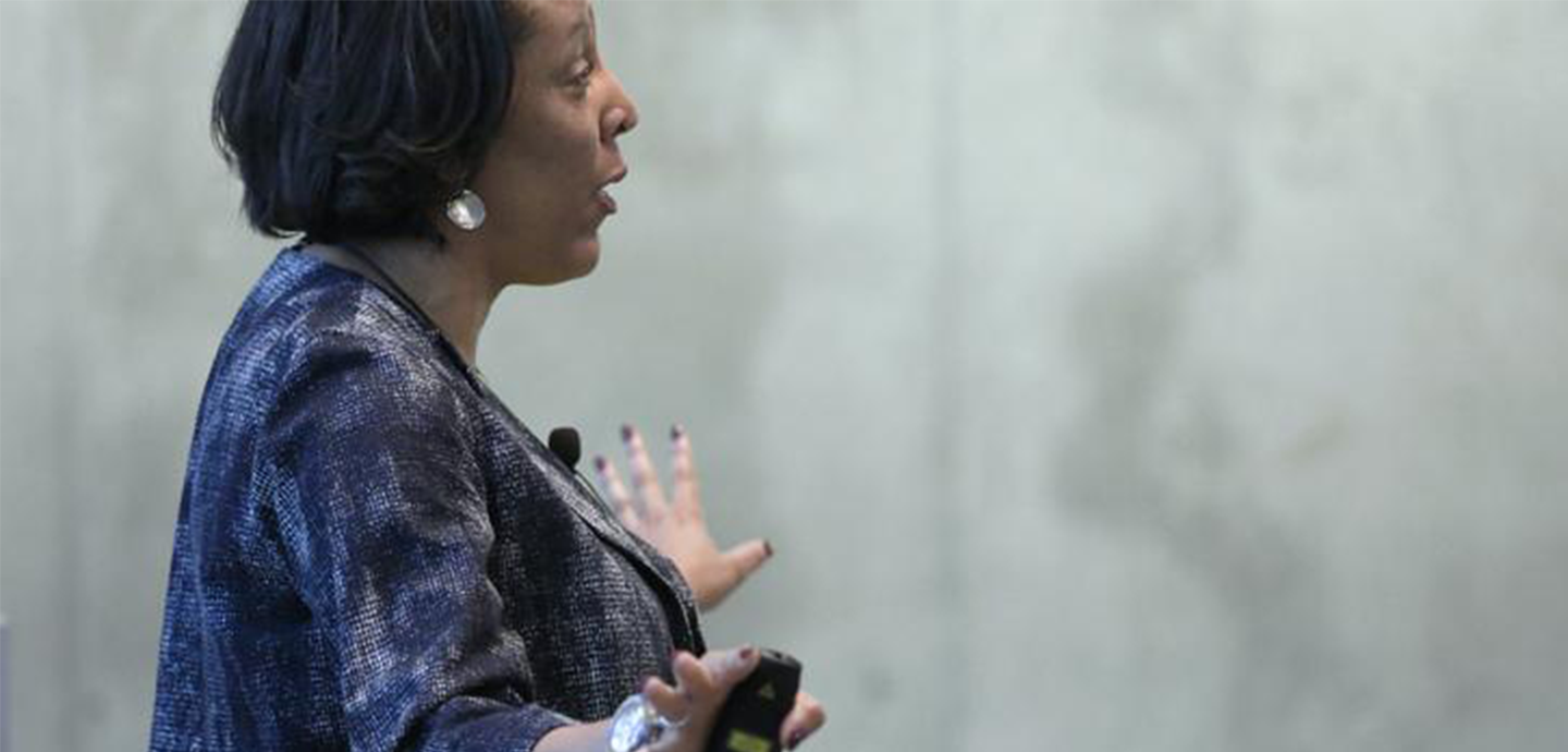 Woman standing with hands pointed outwards with a concrete wall in the background.