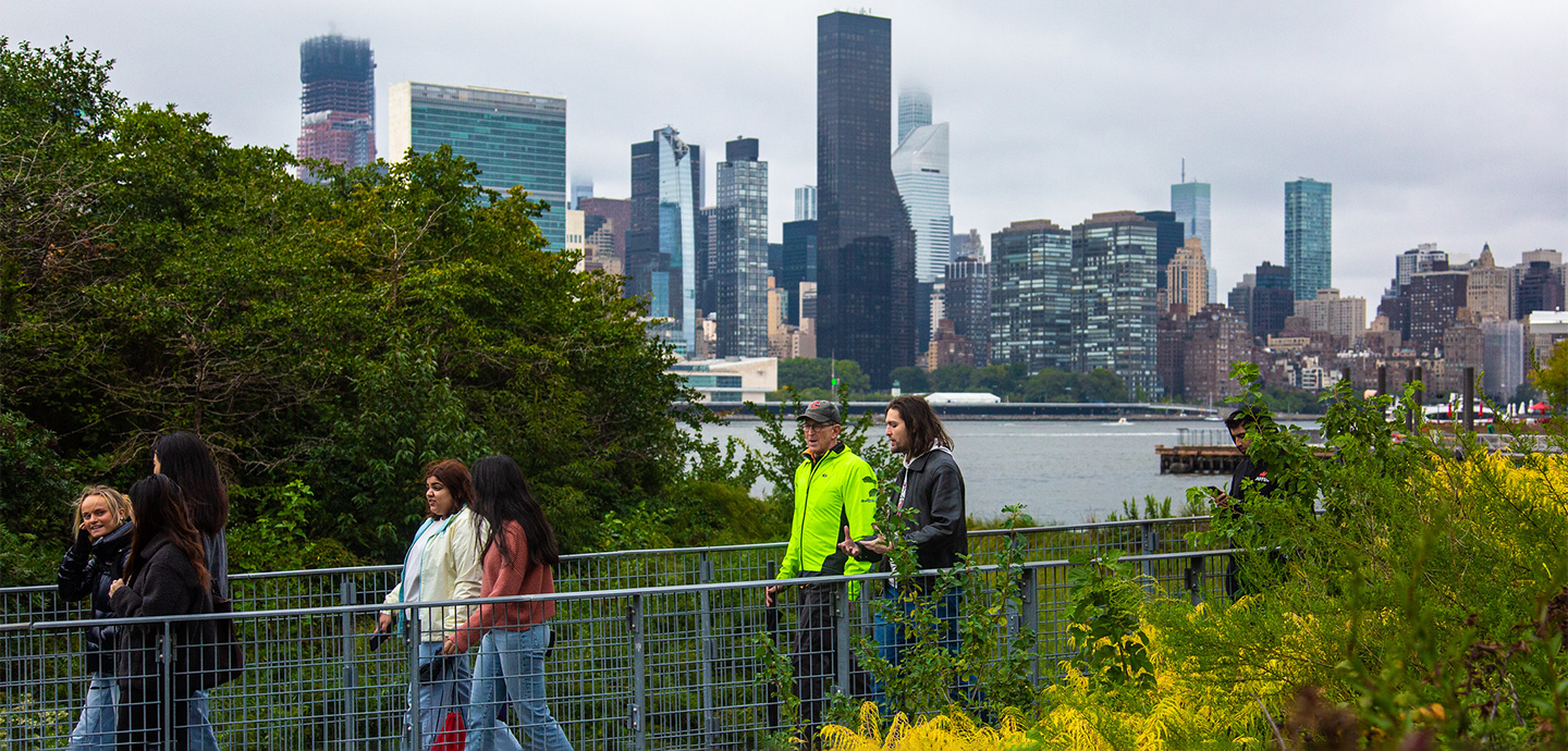 Several peopel walking down a path with a city skyline in the background.