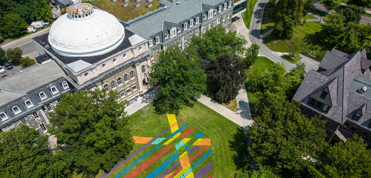 An aerial view of a building with a white dome, trees, and a painted lawns.