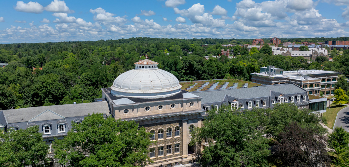 A building featuring a white dome under a blue cloudy sky and surounded by trees.