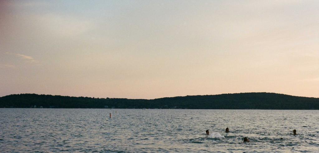 Four people swimming in the water set against a sunset sky with dark land in the background.