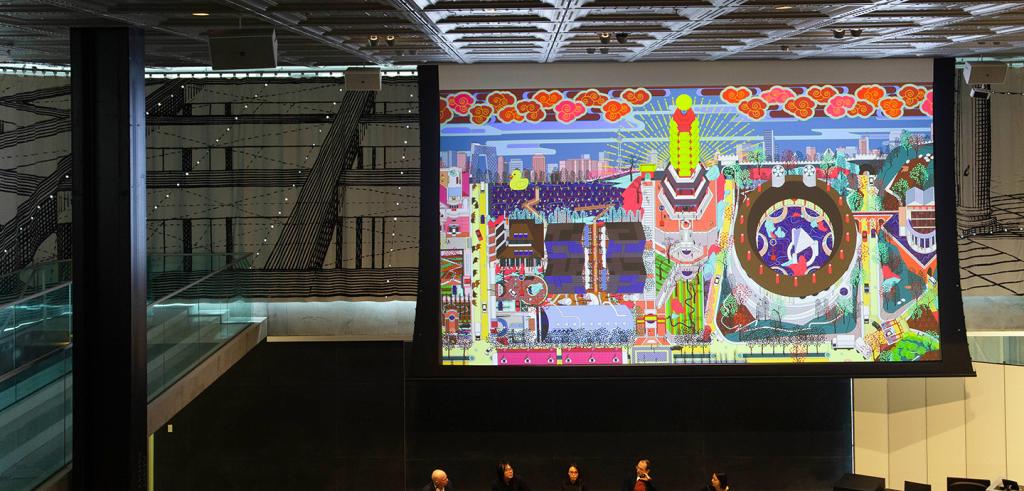 Panelist sitting in the front of an auditorium with a large screen behind them.