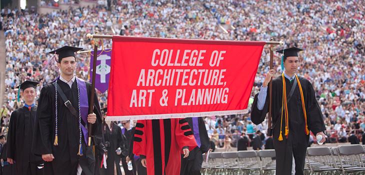 students in cap and gown holding a banner displaying College of Architecture Art and Planning