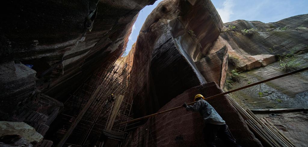 A large rocklike structure with a construction working hauling a large stick.