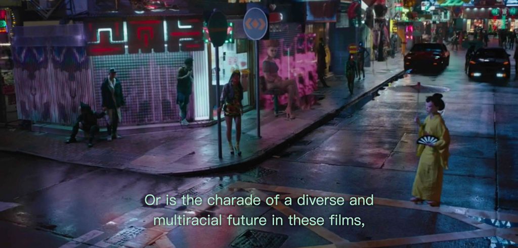 A geisha in a yellow robe with a white paper parasol stands in the street near a street corner with multi-colored lights and signs all around. Subtitles below the geisha read 