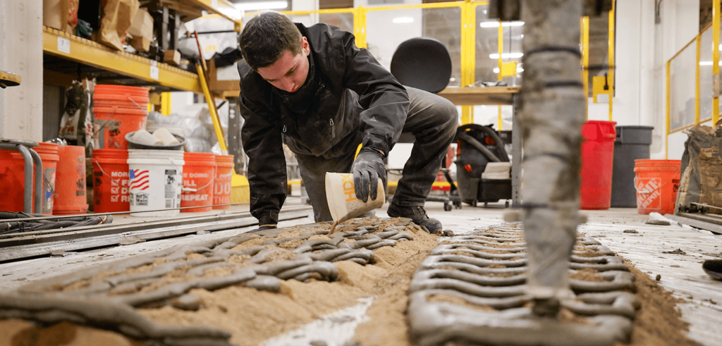 A person pouring sand between extruded concrete structures.