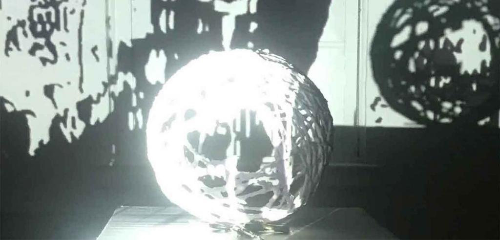 Black and white video still of a ball of yarn on a pedestal with shadows of a ball of yarn in the background.